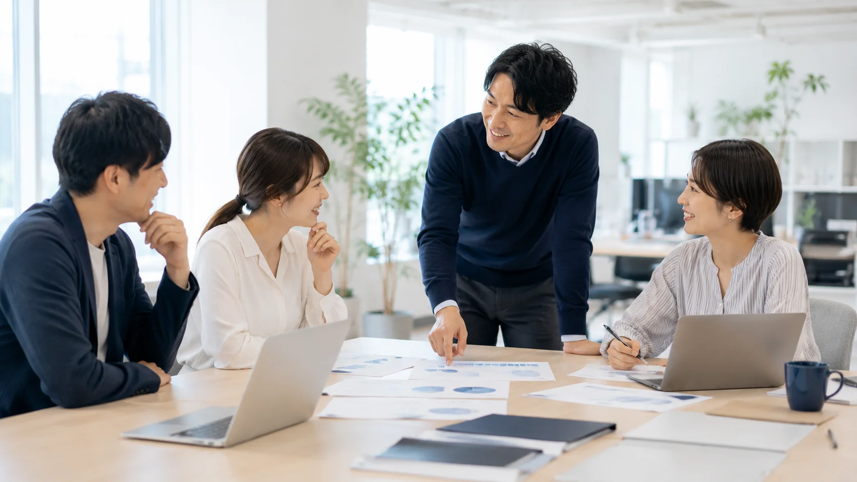 オフィスで和やかに協働する日本人社員たち。人材や組織など非財務的要素が価格に与える影響のイメージ