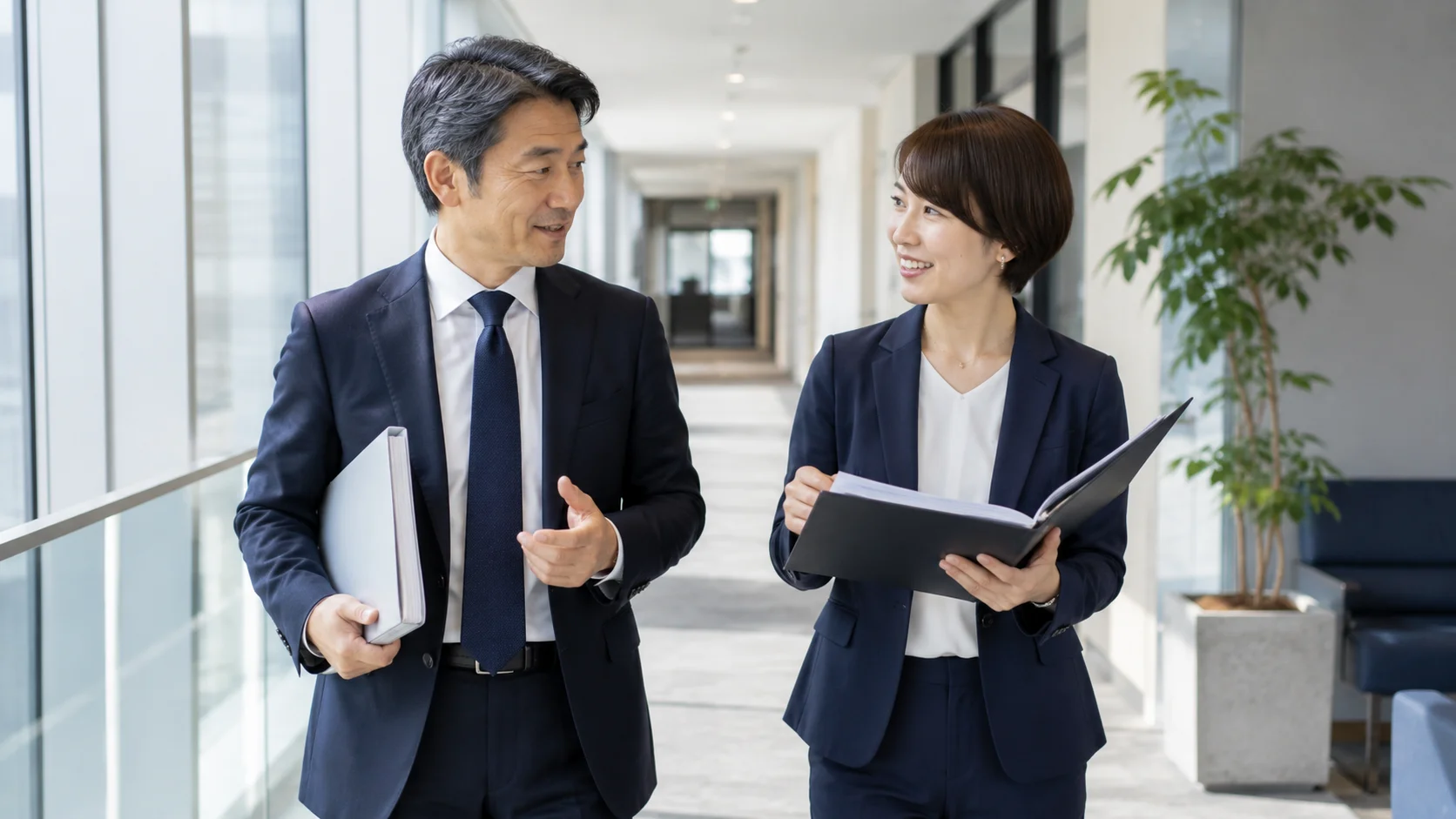 明るいオフィスの通路で対話しながら歩く日本人経営者とアドバイザー、デューデリジェンスを円滑に進めるポイントを表すイメージ